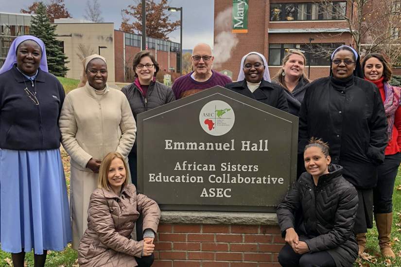 Sr. Draru (left) and ASEC U.S. staff pose for a photo with Sr. Joan Chisala, CSJB (standing, second from right) during her visit to ASEC headquarters in Scranton, PA (Nov. 9, 2018).
