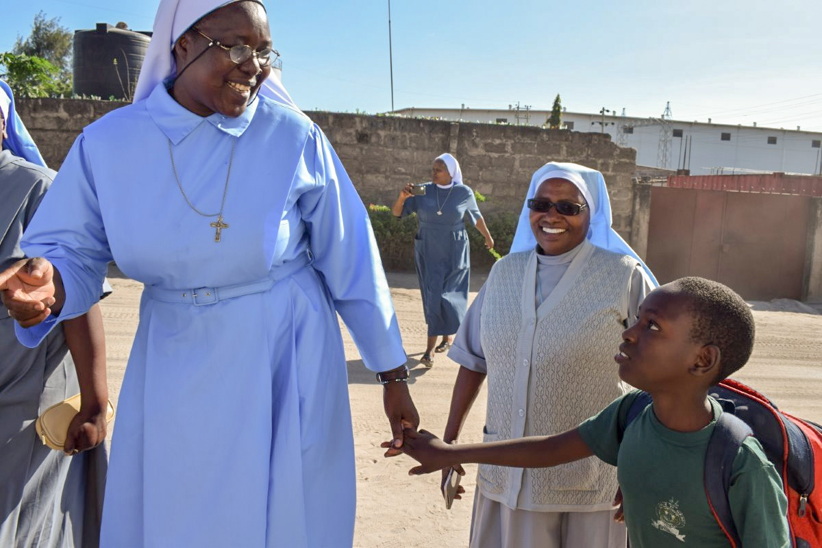 ASEC Executive Director Sr. Draru greets a 9-year-old girl returning from school in Dar es Salaam, Tanzania. They talked about her day at school while they watched the other Sisters sing and dance in the street.